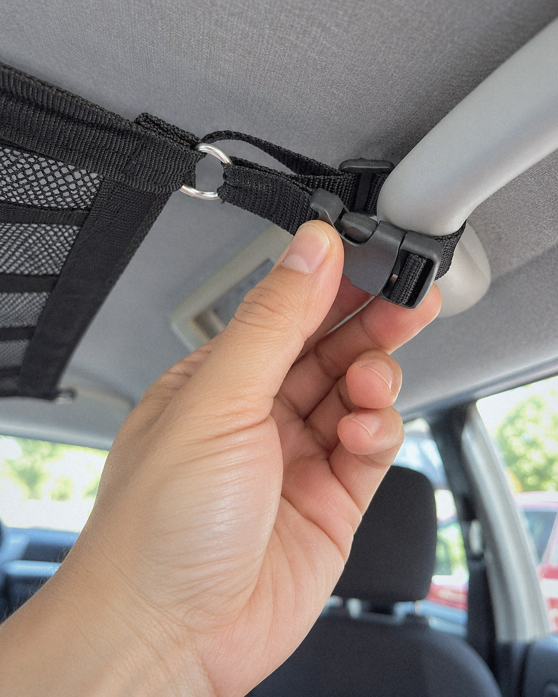 Hand clipping the side-release buckle on a cargo net strap near a grab handle